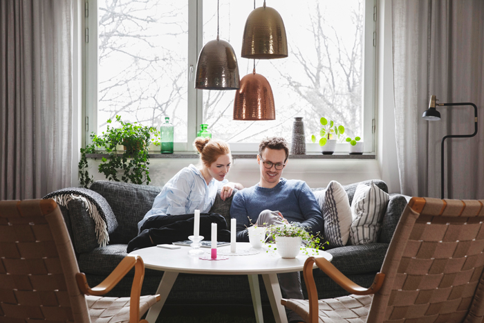 En man och en kvinna sitter i en soffa och tittar på en mobil. De ser glada ut.